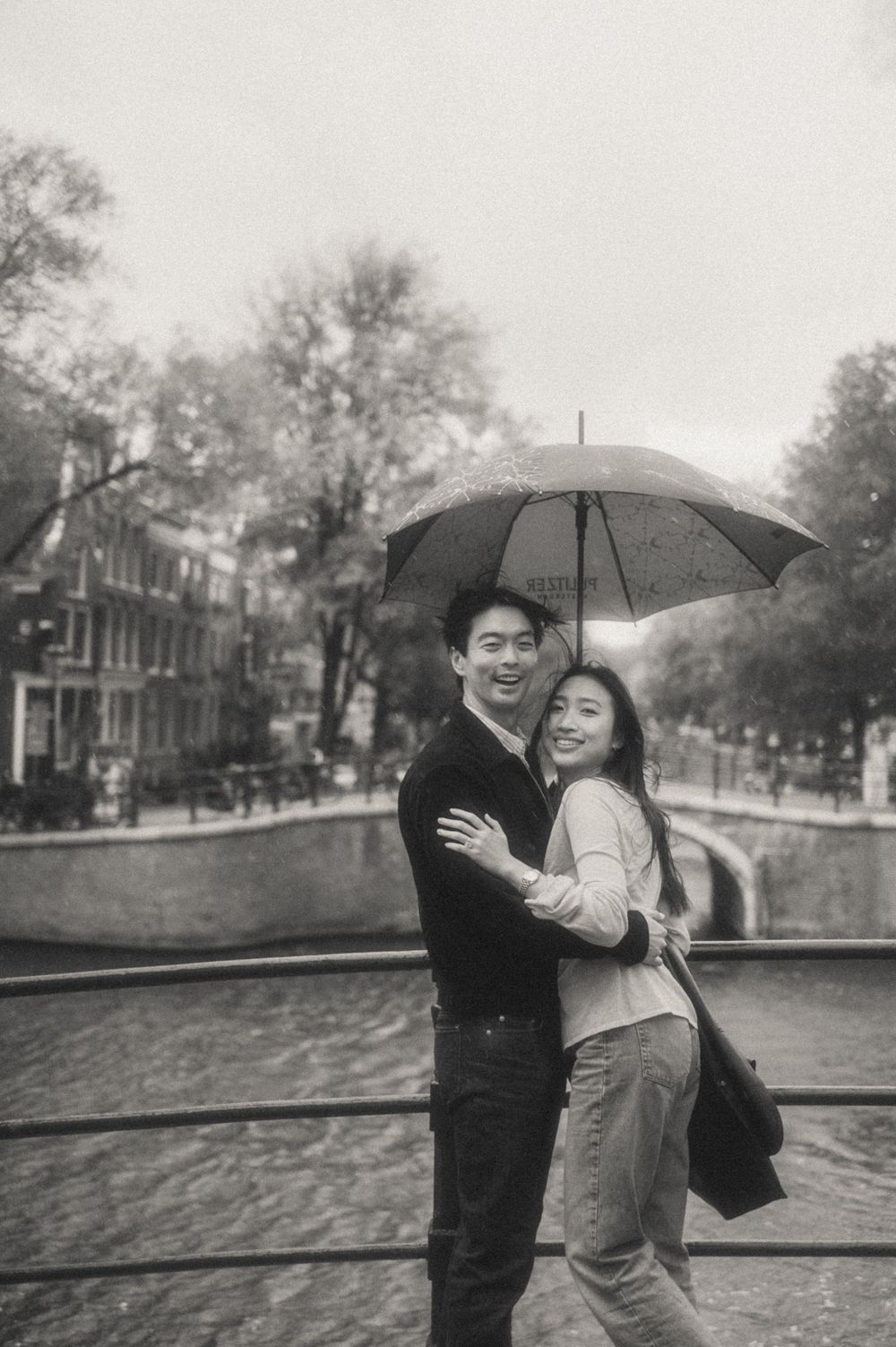 A couple with an umbrella along a canal in Amsterdam during a romantic black and white photoshoot.