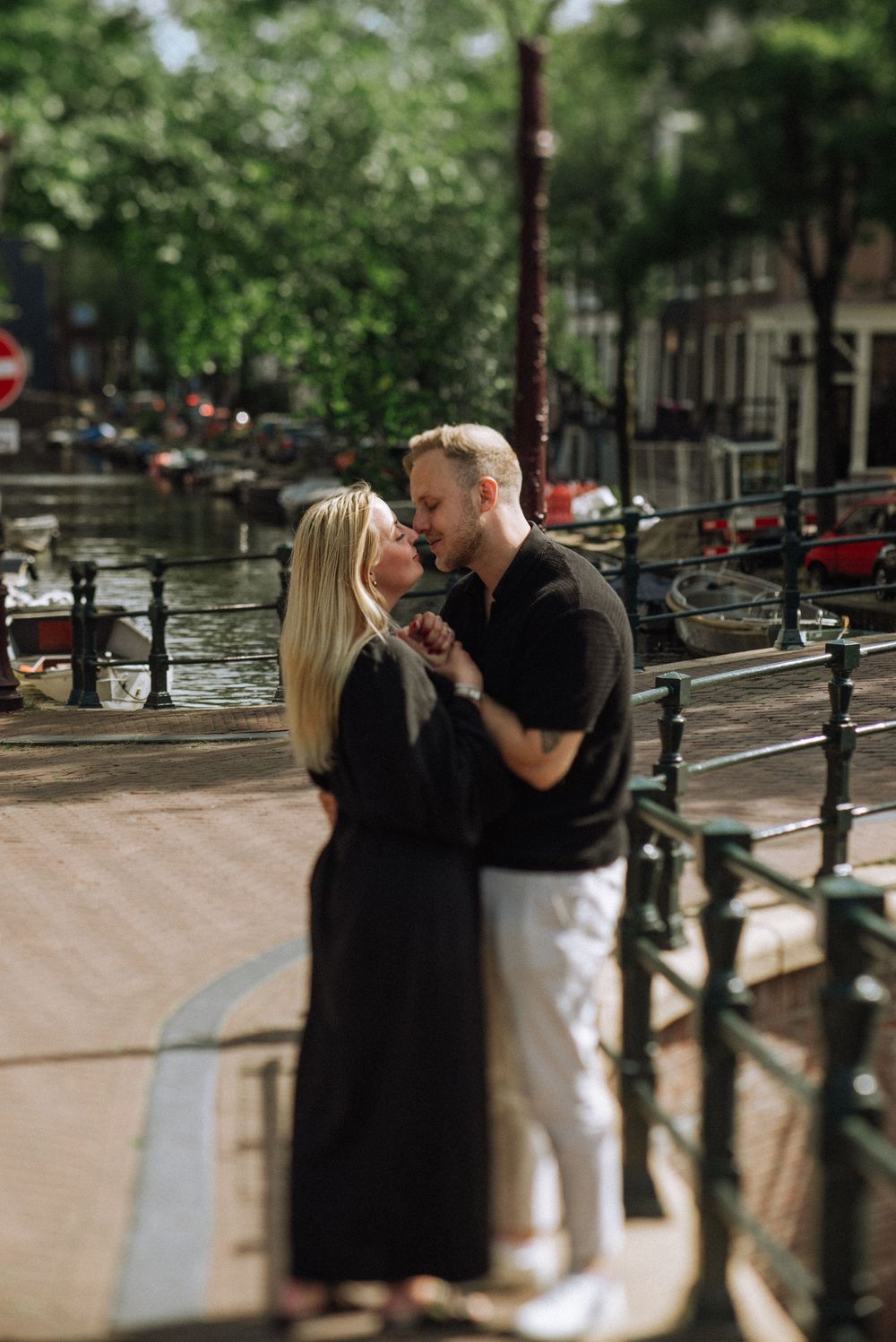 A couple shares a romantic moment along a canal railing in Amsterdam on a summer day.