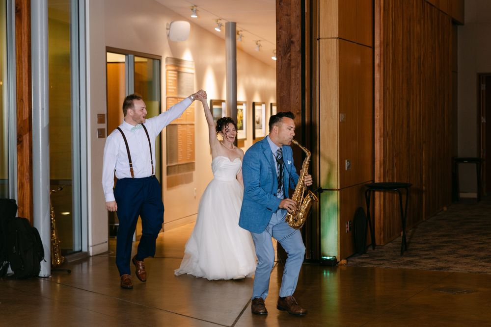 Wedding guests dance and celebrate together in an elegant hallway with warm lighting and wooden paneled walls.