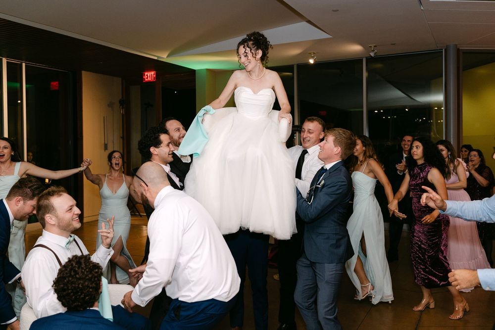 Wedding guests dancing and celebrating on the dance floor at a reception with colorful lighting.