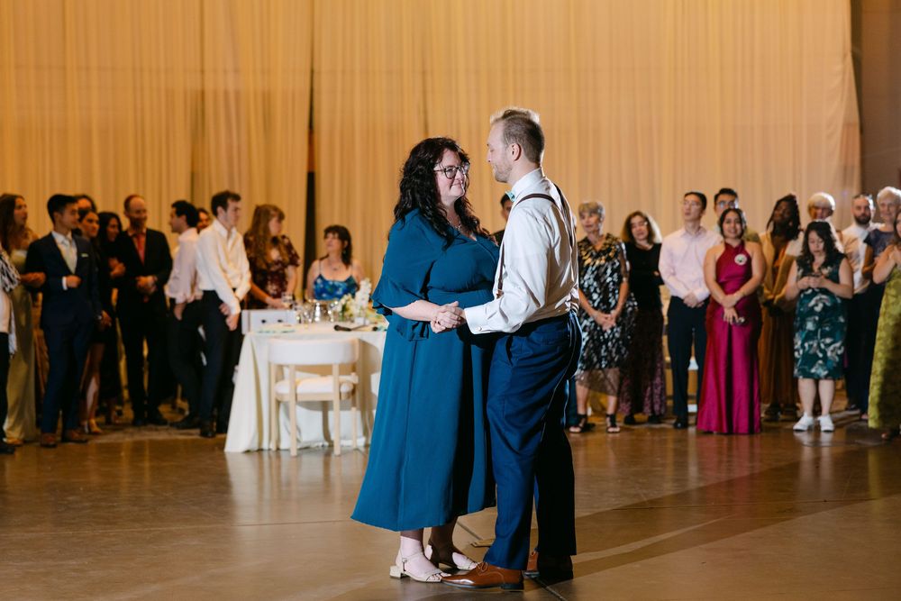 Wedding guests dancing and celebrating on a spacious wooden dance floor at an indoor reception venue.