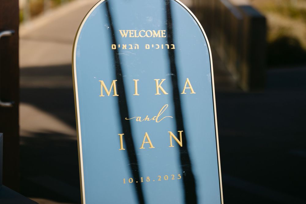 Wedding welcome signs in elegant gold lettering stand displayed at an outdoor venue entrance.