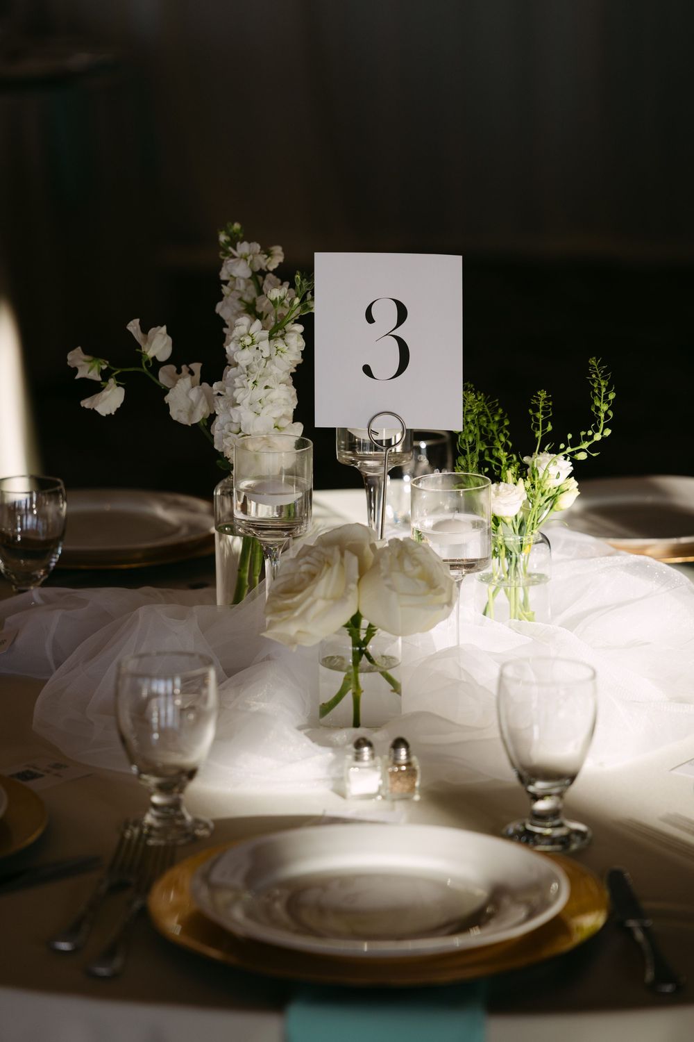 Elegant wedding table settings with white floral centerpieces, table numbers, and glowing candlelight create an intimate atmosphere.