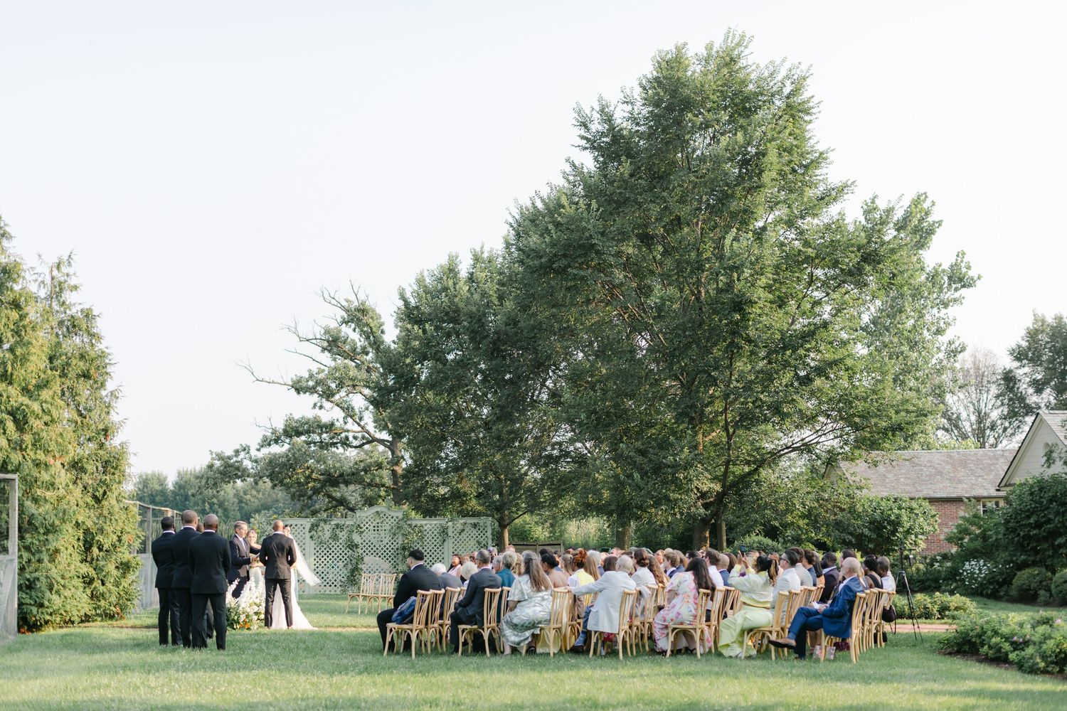 Wedding guests gather on a lush green lawn during an outdoor summer ceremony. - Elawa Farm