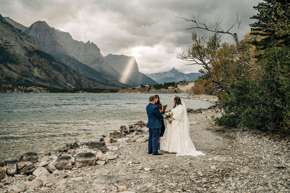 A mountain lake wedding ceremony on rising sun picnic area shoreline with dramatic cloudy skies and rocky shoreline in the background.