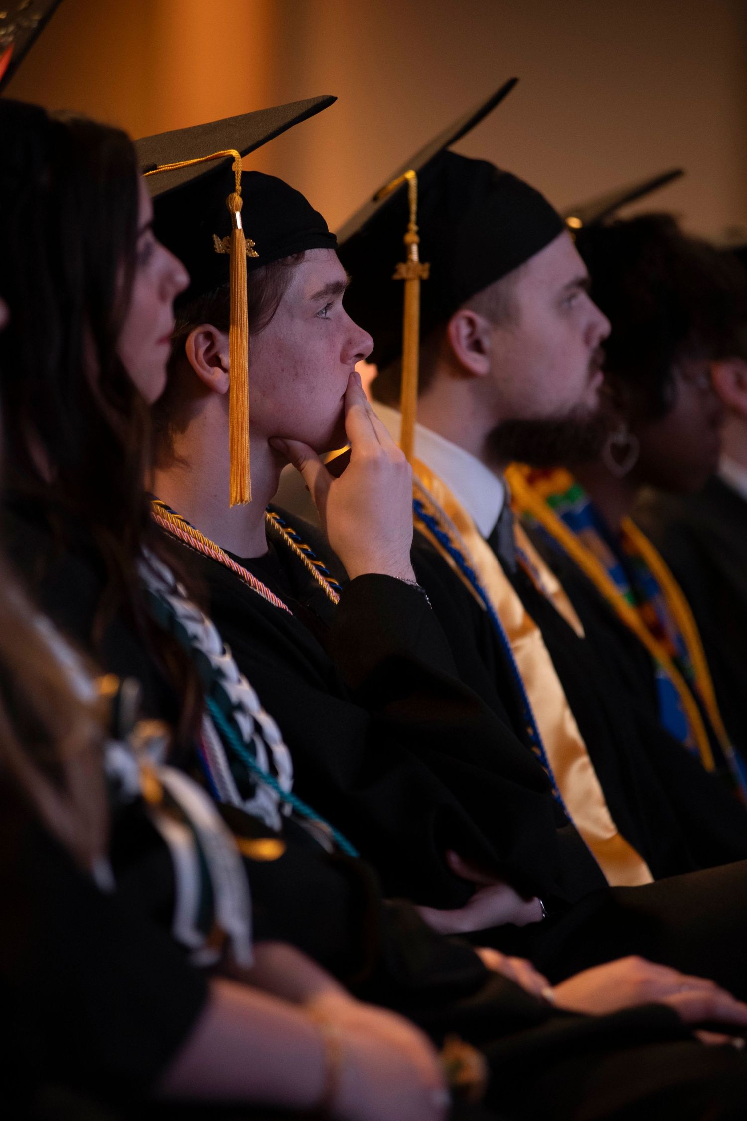 Graduate in black cap and gown poses against blue backdrop in professional graduation portrait series.