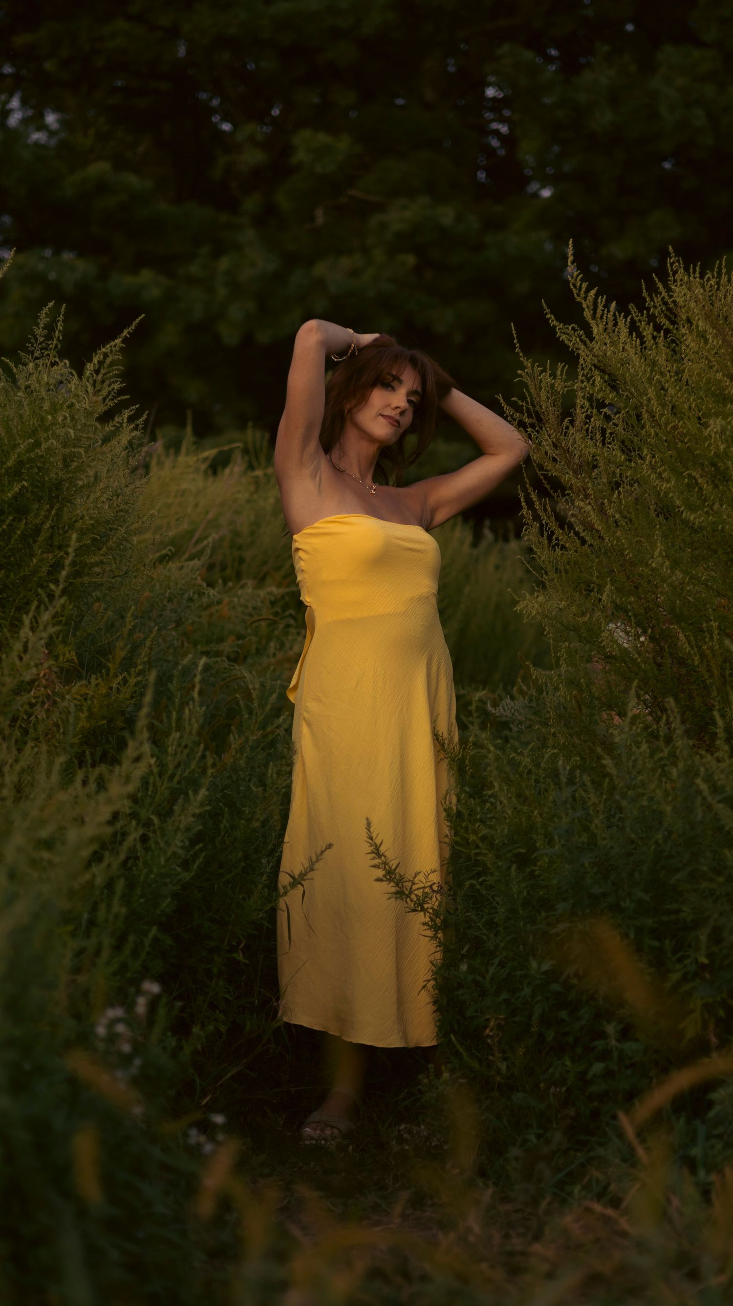 A figure in a flowing yellow sundress poses gracefully among tall wildflowers at sunset.