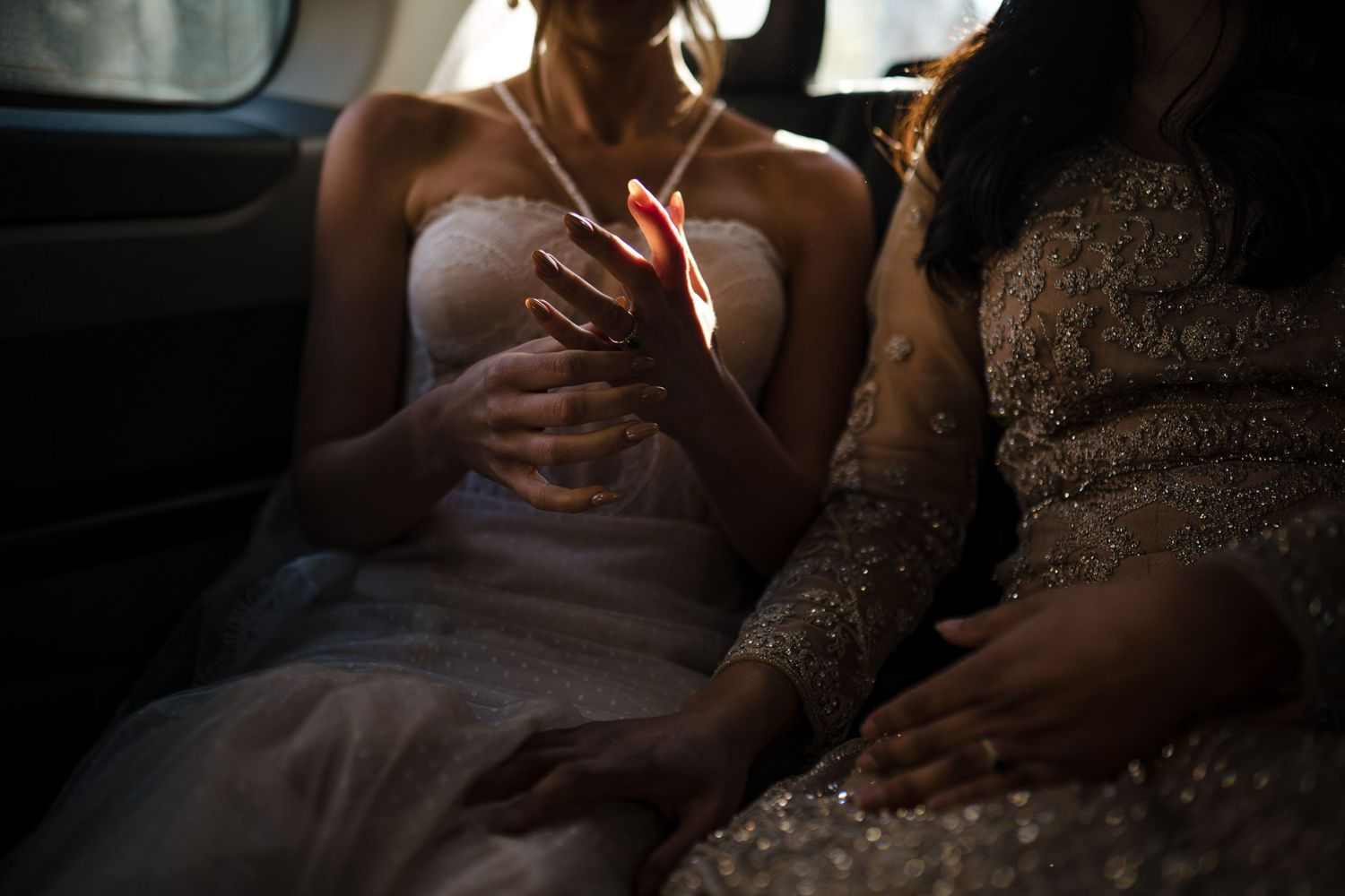 Two brides in wedding dresses sit together in the backseat of a car illuminated by soft natural light driving to The Lord Nelson, Halifax.