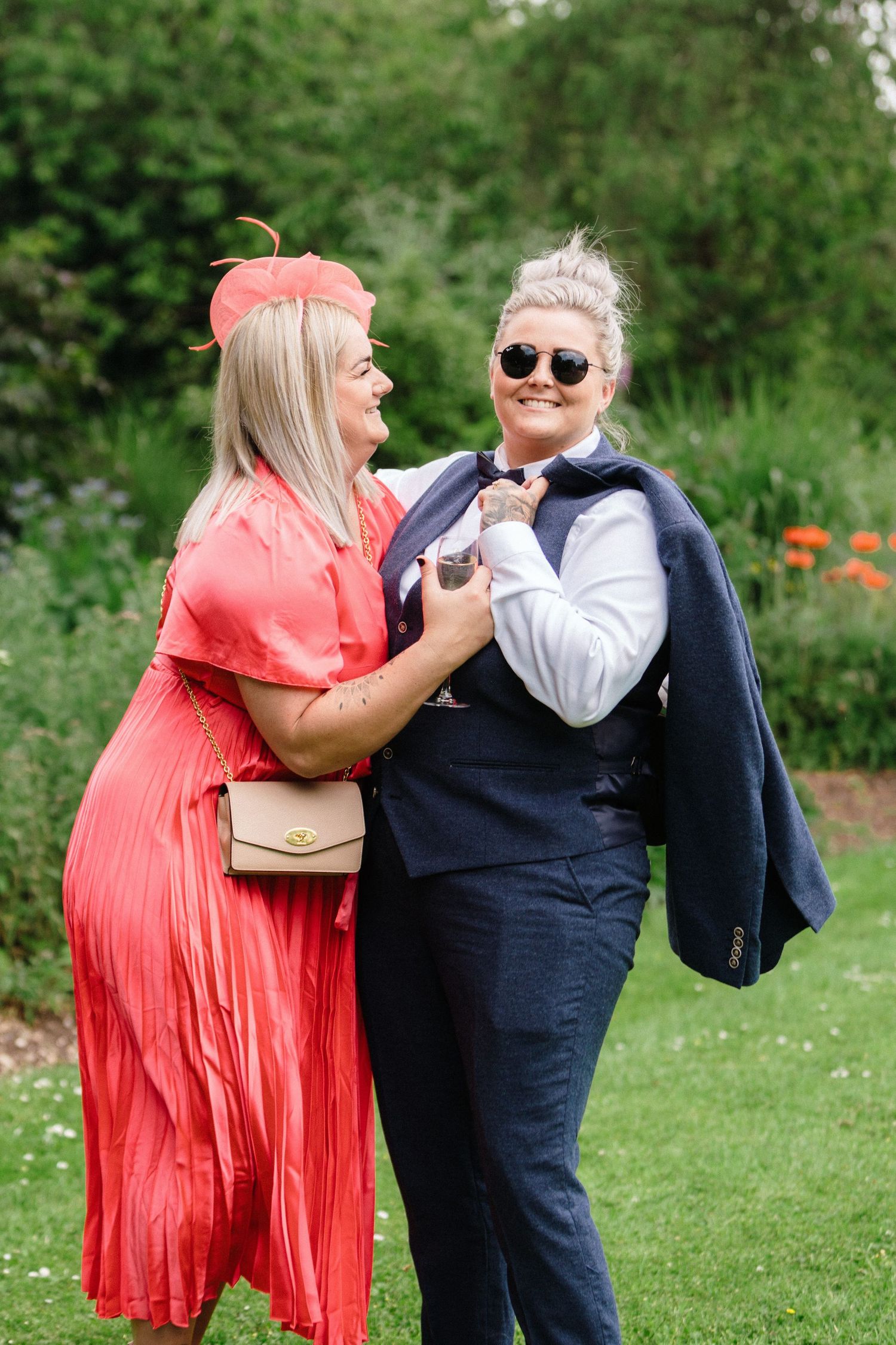 LGBTQ couple laughing together at an outdoor wedding one wearing coral dress and another in navy suit near The Lord Nelson, Halifax