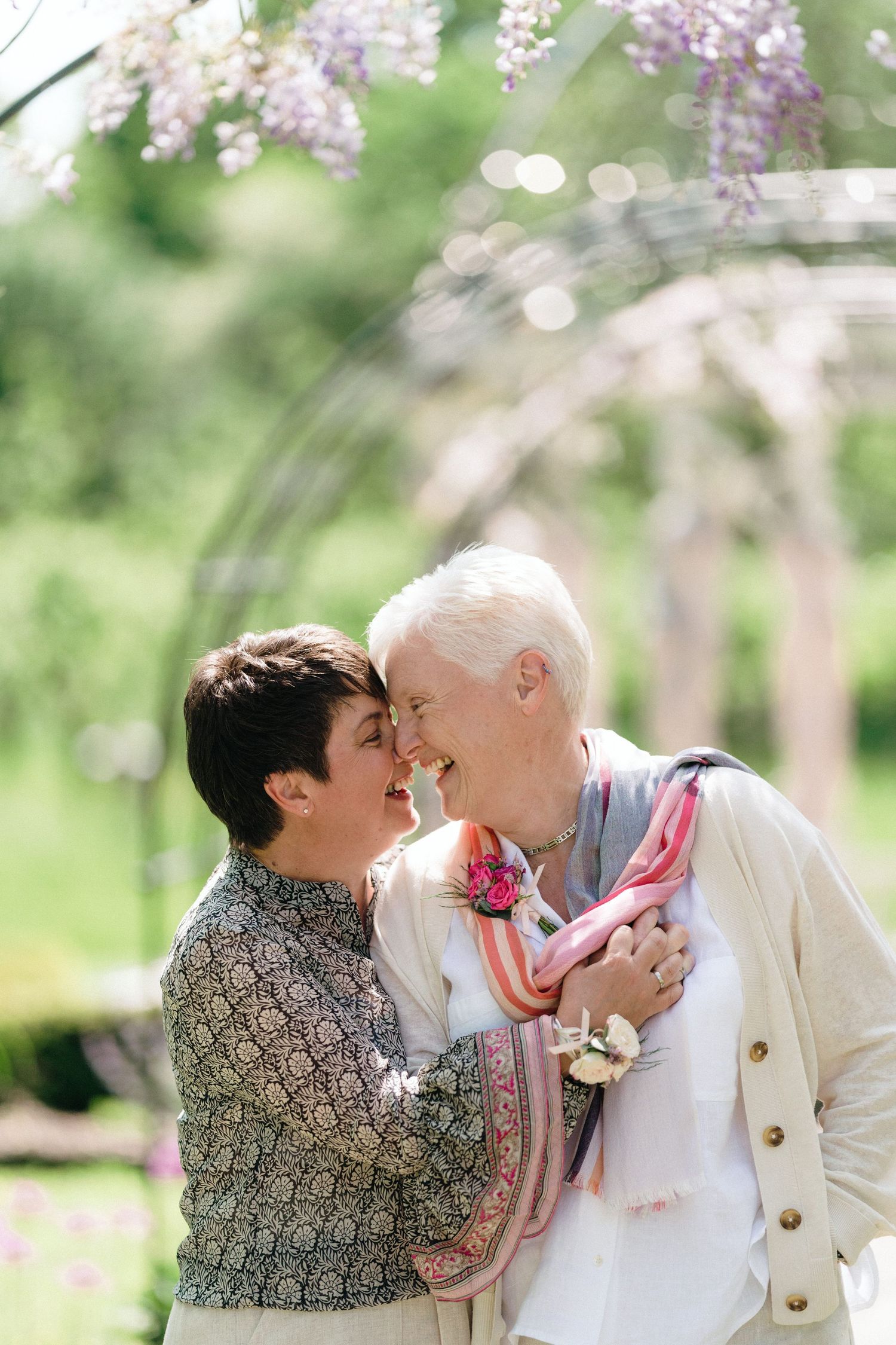 LGBTQ couple embracing under blooming wisteria in spring garden setting near The Lord Nelson, Halifax wedding venue.