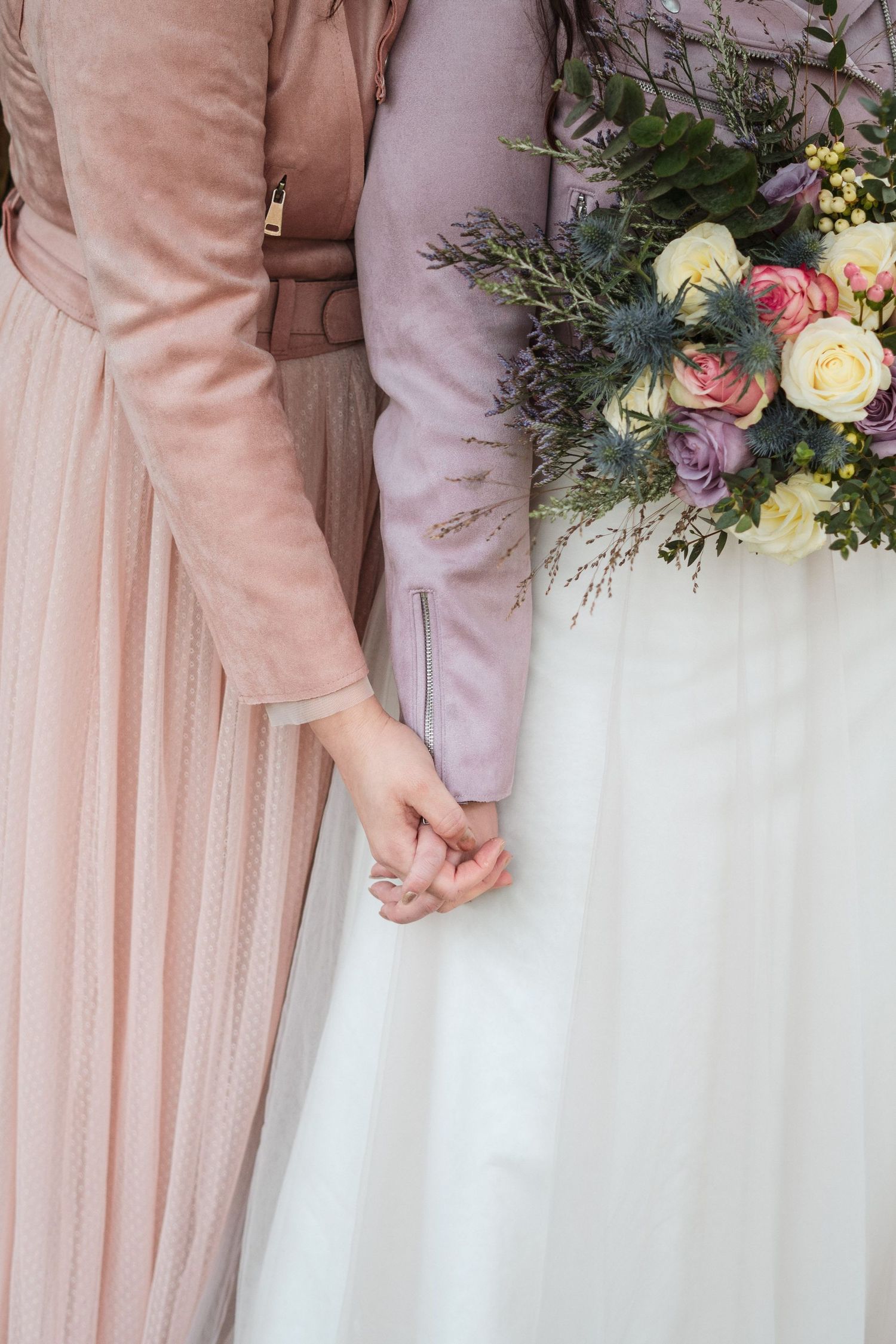 Close-up of two LGBTQ brides holding hands with pastel wedding bouquet and gowns at The Lord Nelson, Halifax wedding venue.