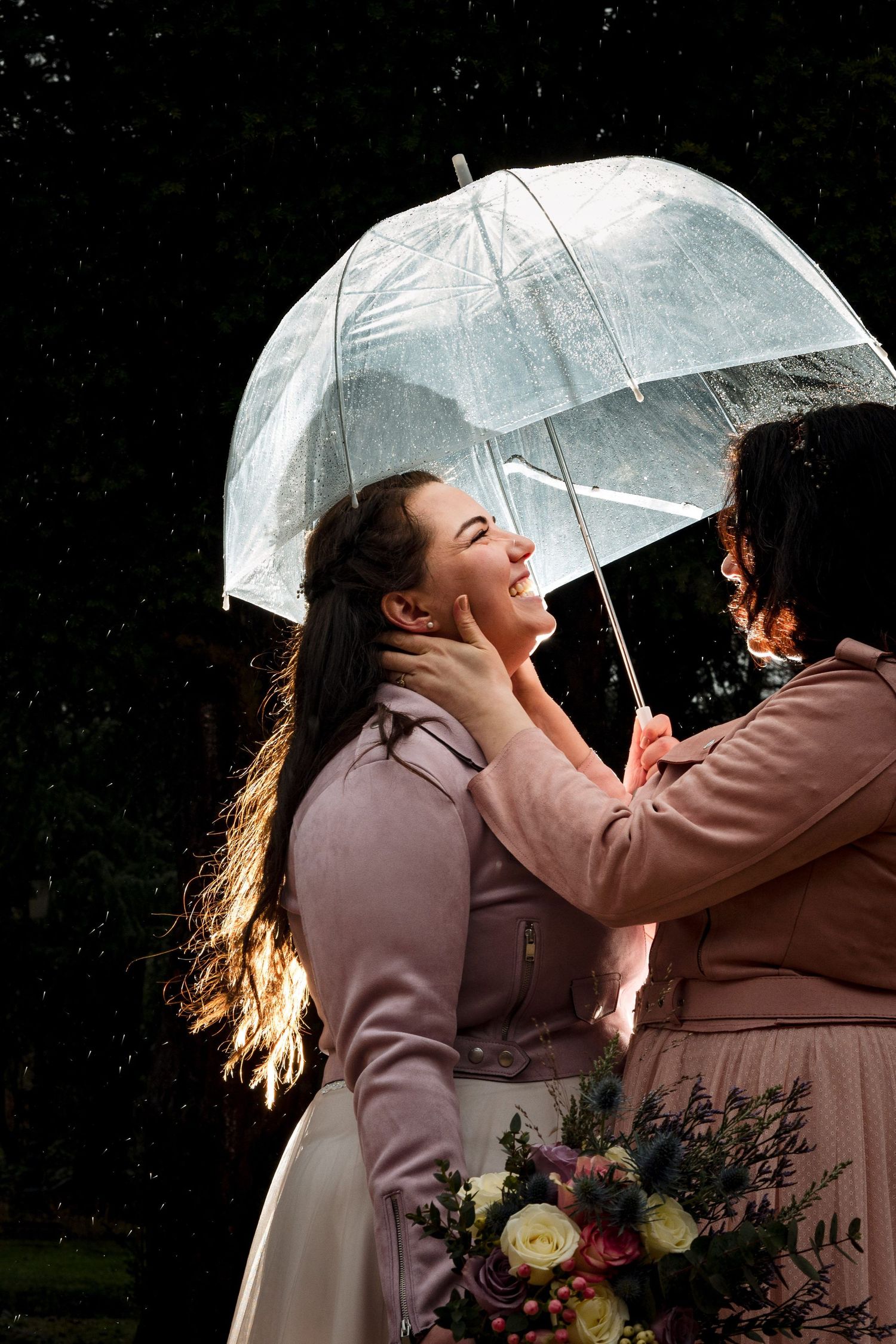 Joyful moment shared under a clear umbrella in the rain as a LGBTQ couple embrace near The Lord Nelson, Halifax wedding venue.