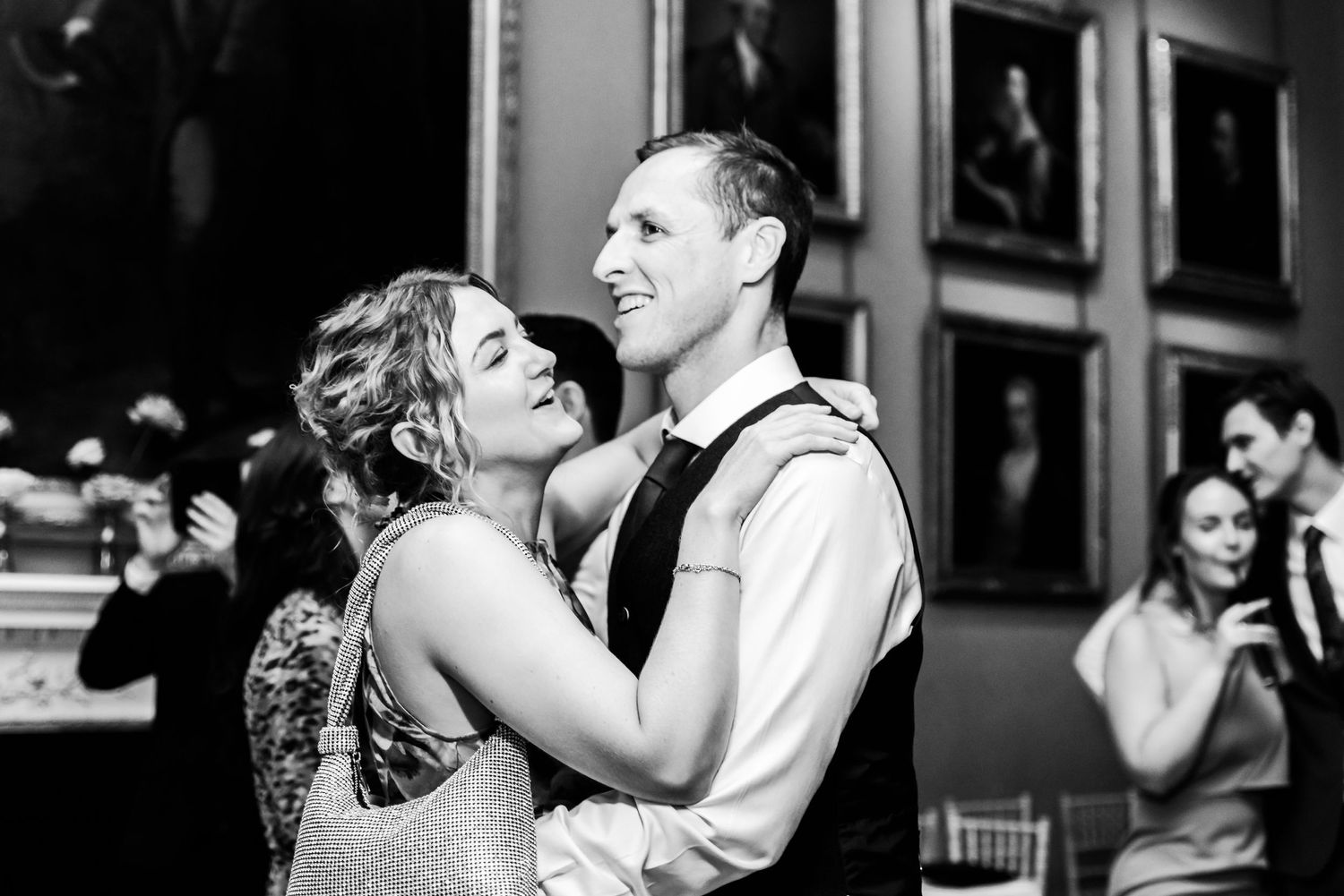 A joyful couple shares a romantic dance moment together at an elegant reception venue in black and white photography.