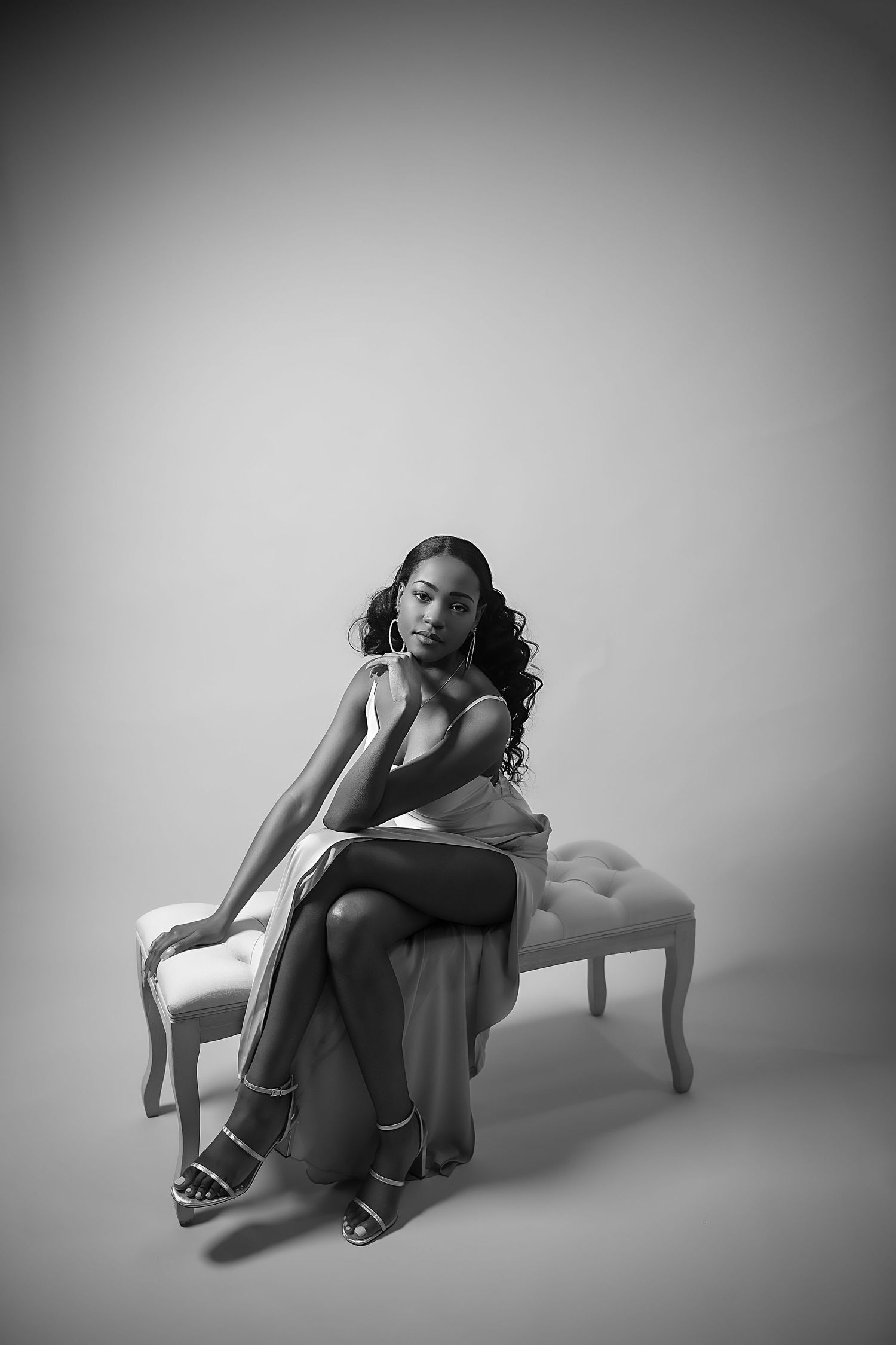 Artistic black and white portrait of woman posed on tufted bench.