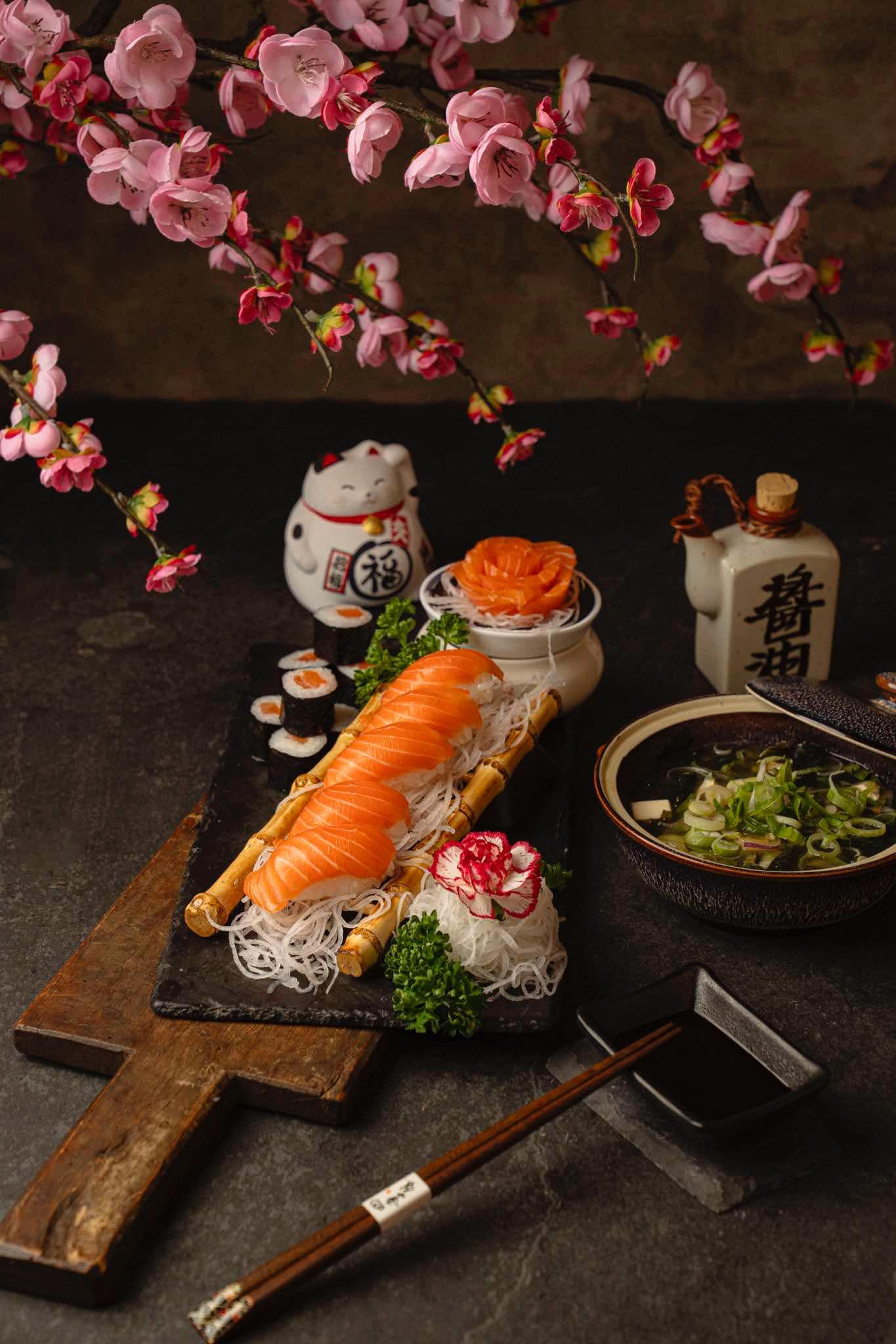 Fresh sushi and sashimi platter with cherry blossoms and sake bottle on dark wooden board.