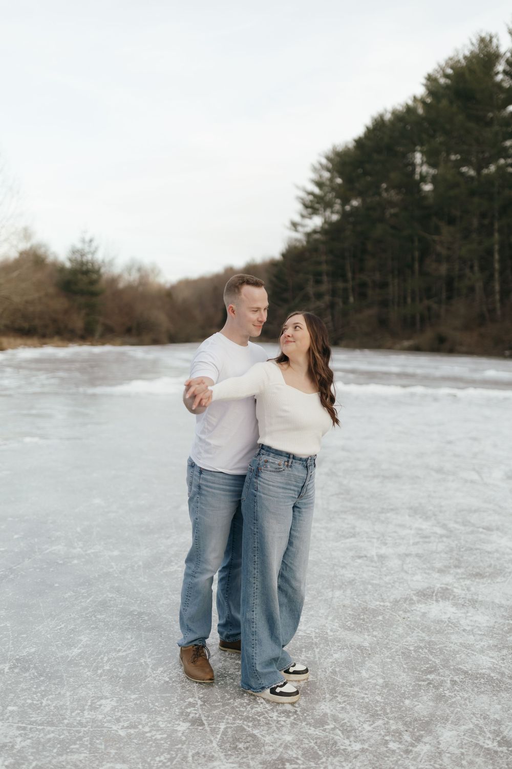 Couple dancing together on frozen lake surrounded by winter forest landscape.