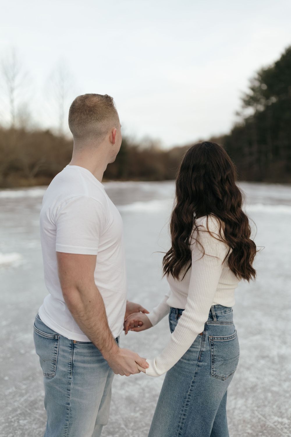 Couple in casual winter outfits standing on frozen lake from behind.