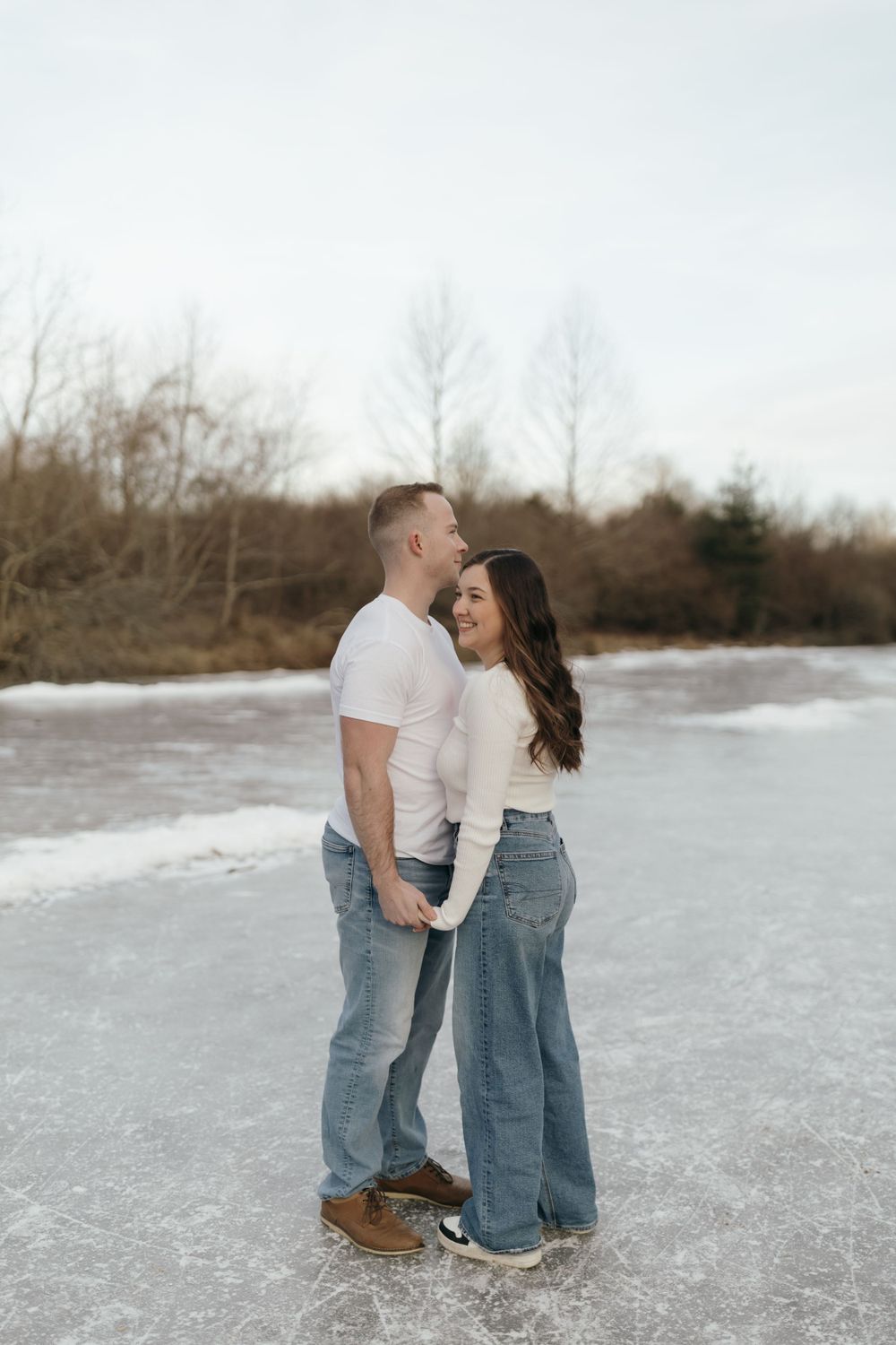 Intimate couple portrait on frozen lake with winter trees in background.