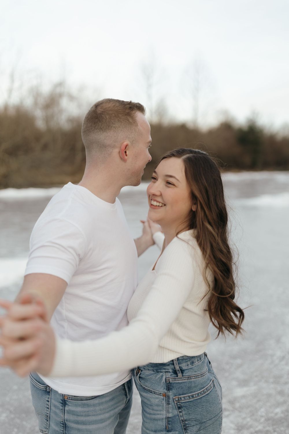 Joyful couple laughing while embracing on frozen lake.
