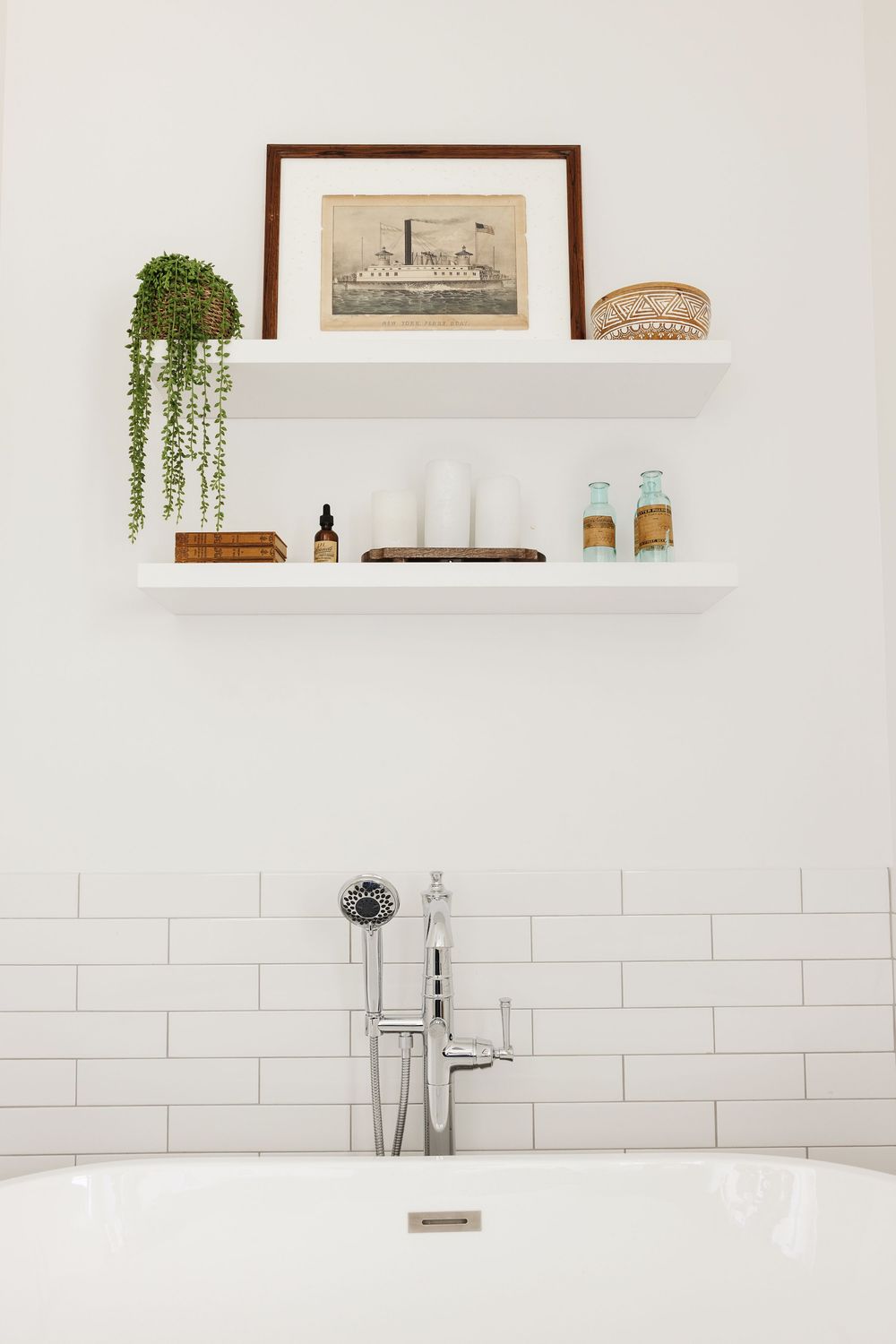 White bathroom shelves with plants and decor above a freestanding bathtub with chrome faucet or an AirBnb listing on Fire Island..