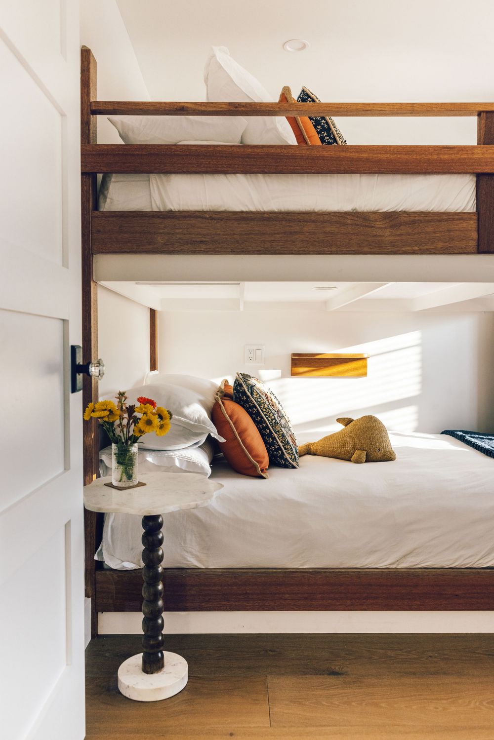 Wooden bunk beds with colorful pillows and a small side table with yellow flowers or an AirBnb listing on Fire Island..