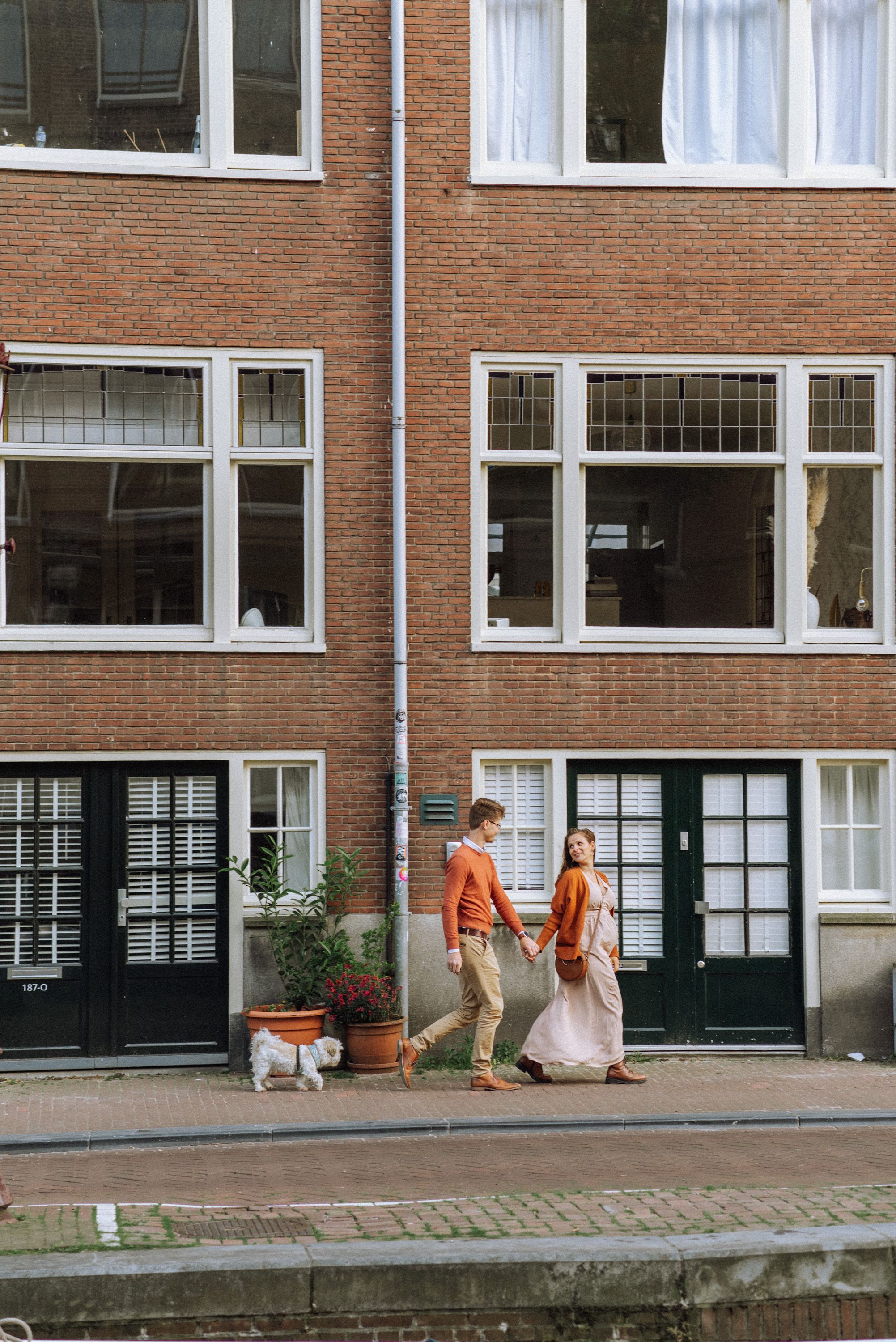 Orange chairs line the exterior of a brick apartment building with large windows.