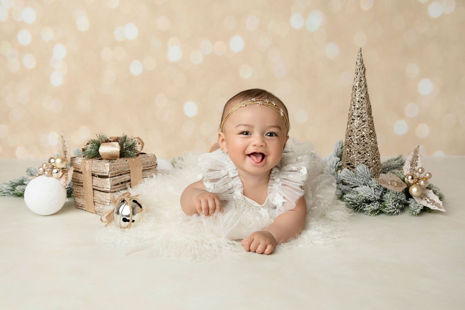 Holiday themed baby photo with silver tree decor and winter props on light background.