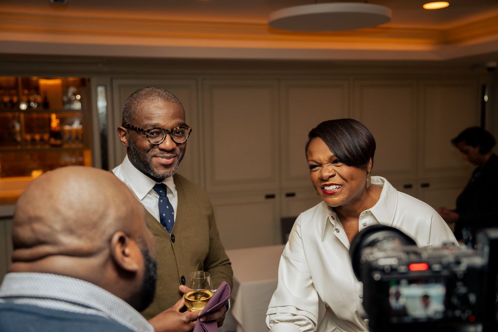 People share a lighthearted moment while being filmed at an indoor event.