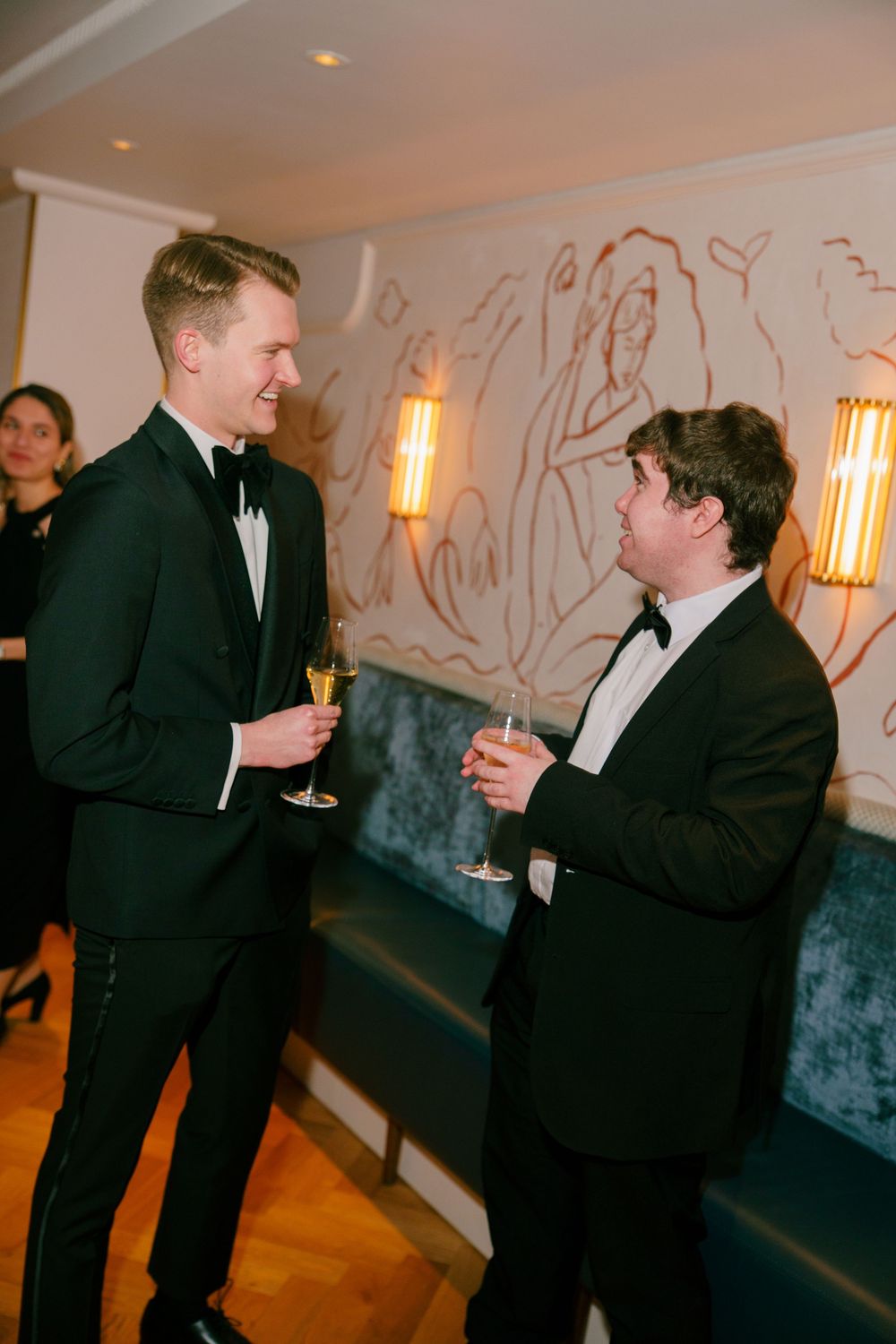 Two men in black tuxedos toasting with champagne glasses at an elegant evening event.