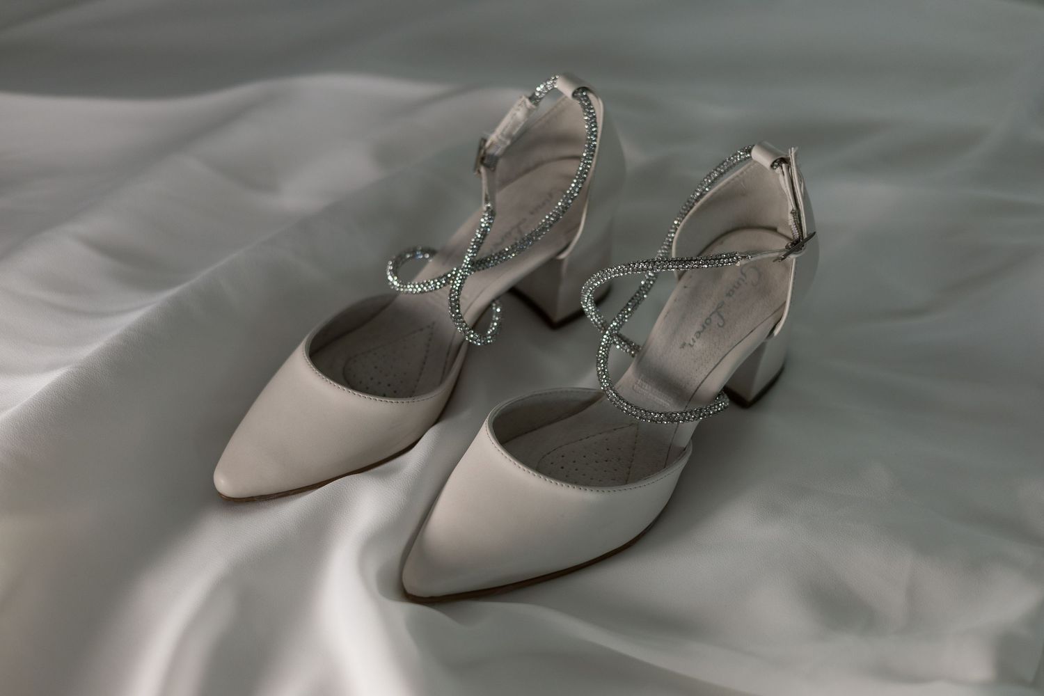 Elegant silver bridal shoes displayed on soft gray fabric.