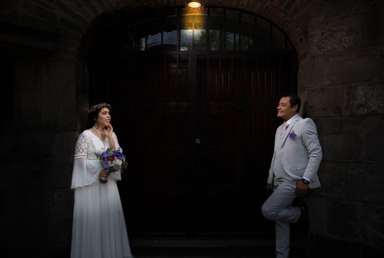 Romantic wedding photoshoot in a dimly lit brick-walled venue with dramatic lighting.