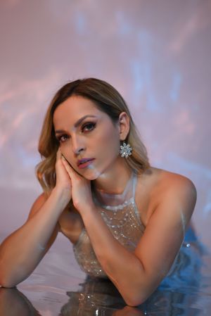 Woman in sparkling dress with elaborate jewelry posing against soft pink backdrop.