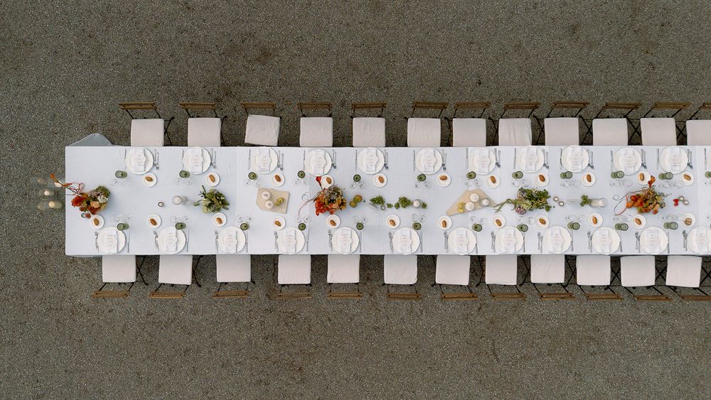 Aerial view of a long white wedding reception table with floral centerpieces set against a concrete background.
