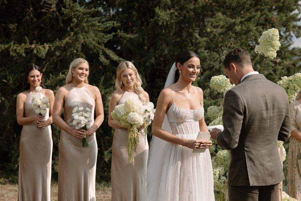 Wedding ceremony in progress with bridesmaids in neutral dresses holding white bouquets.