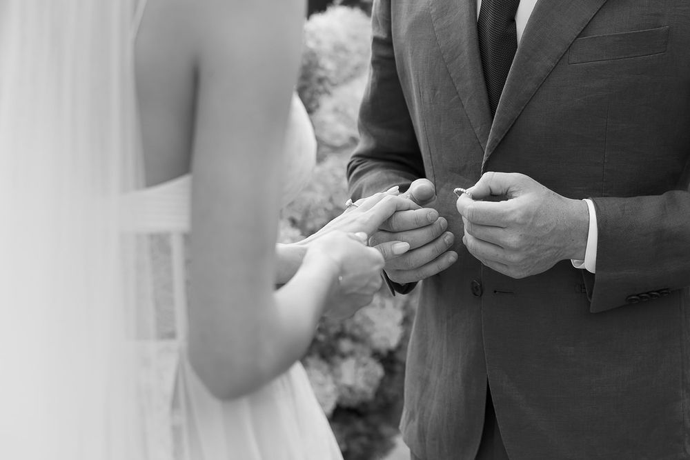 Close-up black and white shot of couple exchanging wedding rings during ceremony.