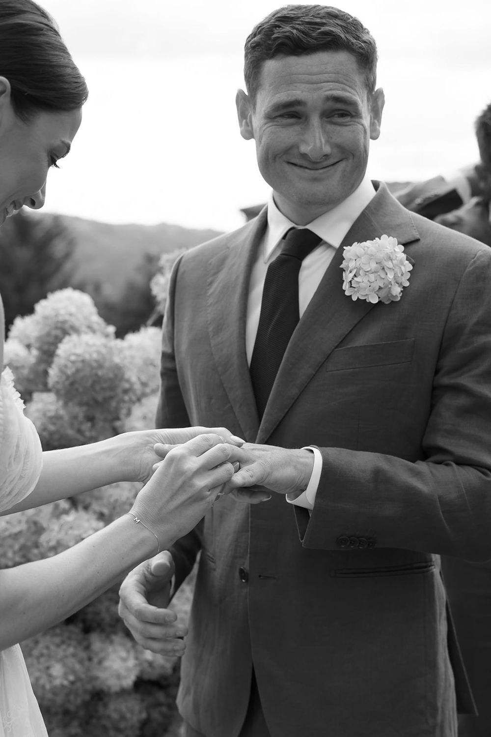 Black and white photo of wedding ring exchange against mountain backdrop.