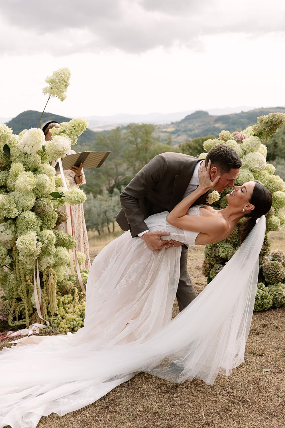 Romantic wedding couple sharing intimate moment with flowing veil against mountain landscape.