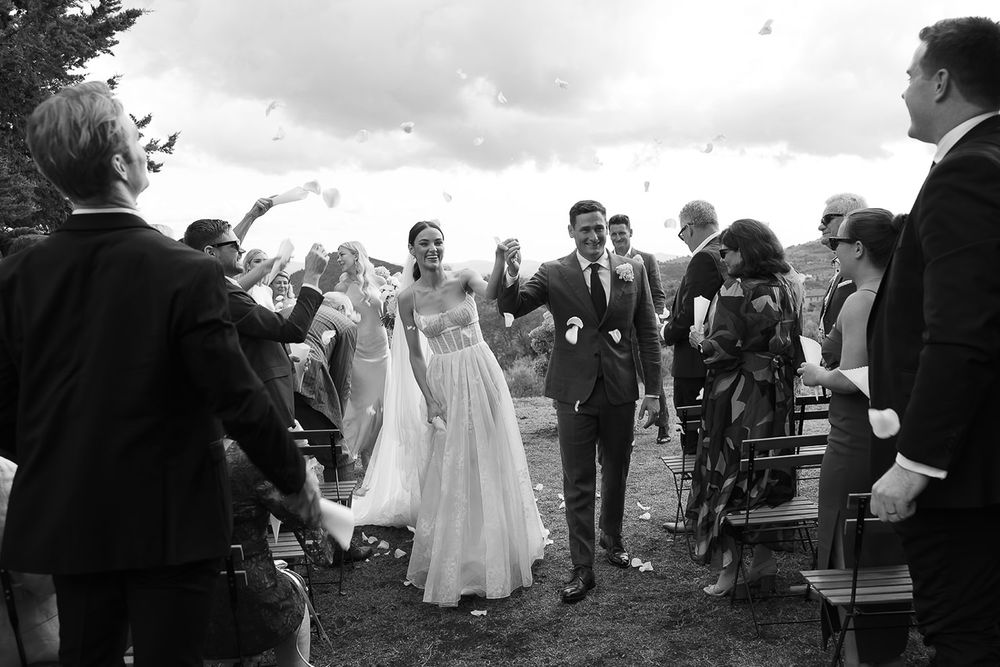Wedding exit with guests tossing confetti as couple walks through in black and white.