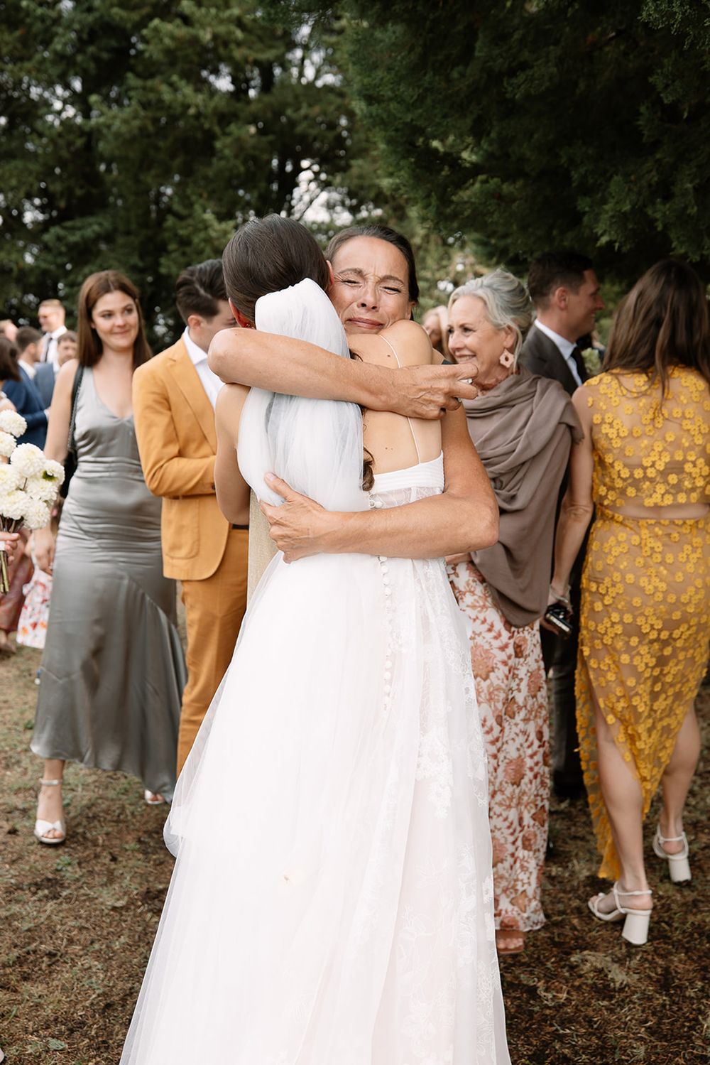 Warm embrace between two wedding guests wearing formal attire at an outdoor celebration.