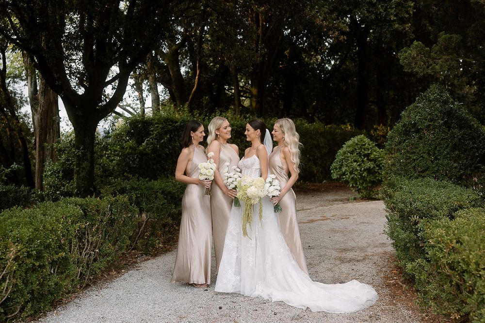 Wedding group walking along gravel path surrounded by manicured garden hedges and trees.