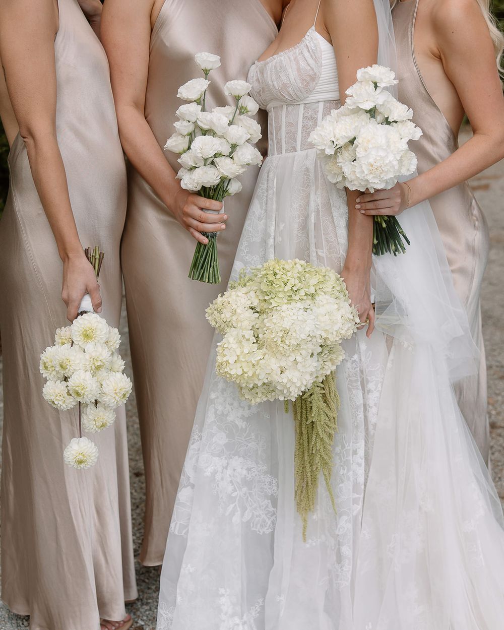 Close up of wedding bouquets with white roses and hydrangeas held against blush and white dresses.