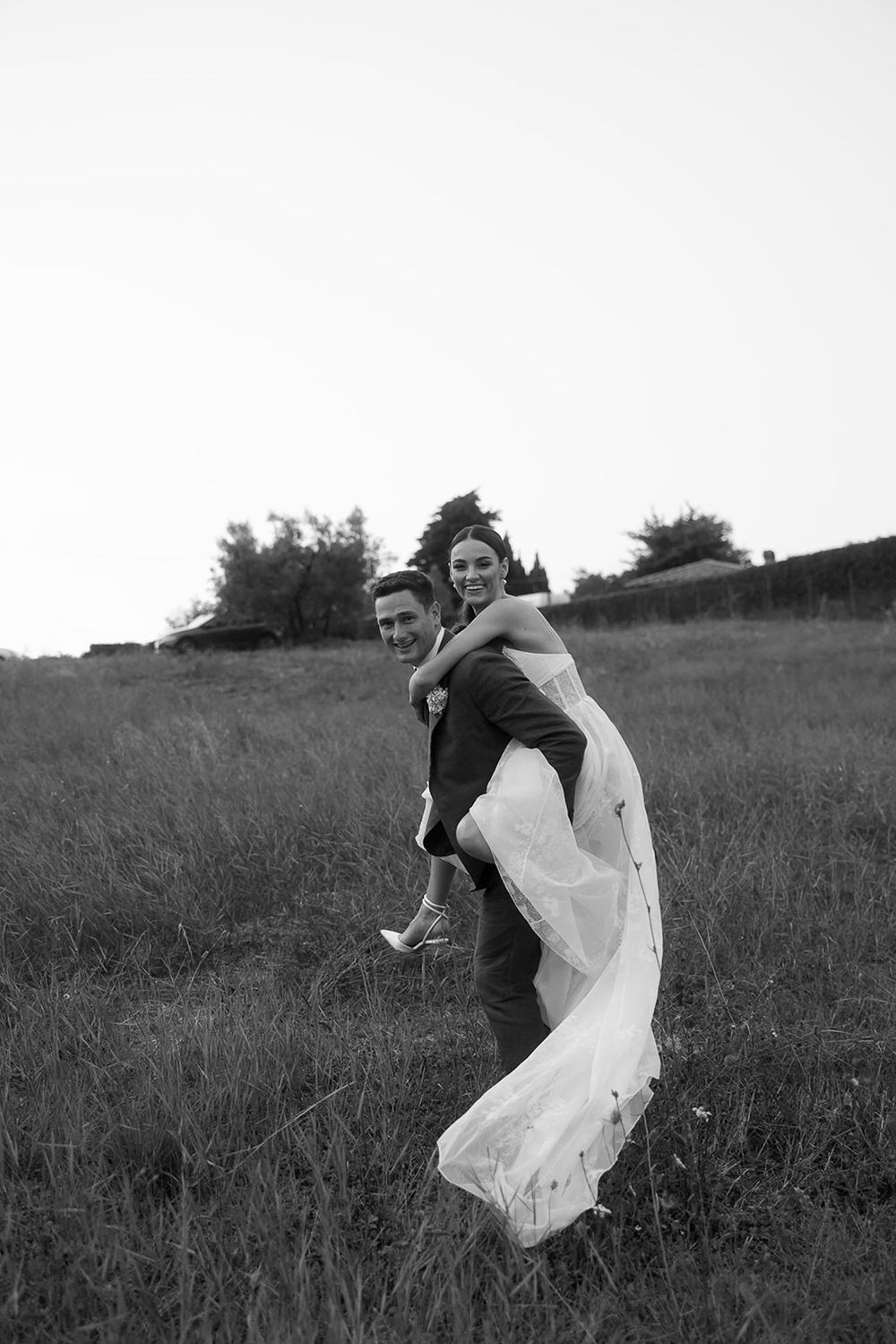 Black and white portrait of playful piggyback moment in a grassy field.
