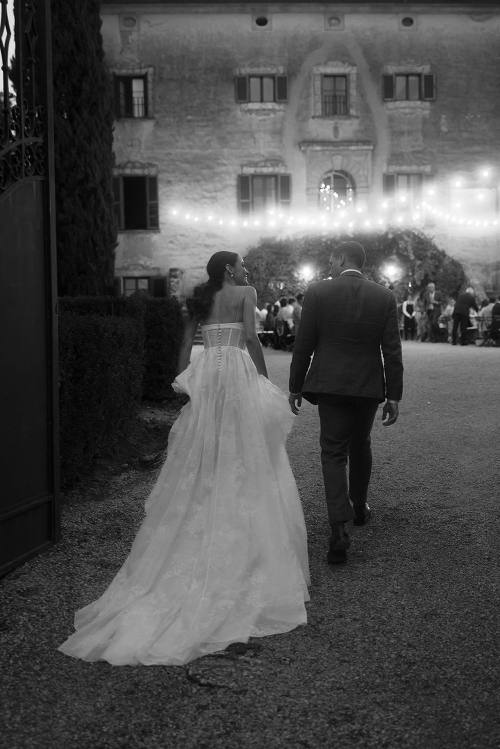 Black and white photo of couple walking toward Italian villa with flowing wedding dress train.