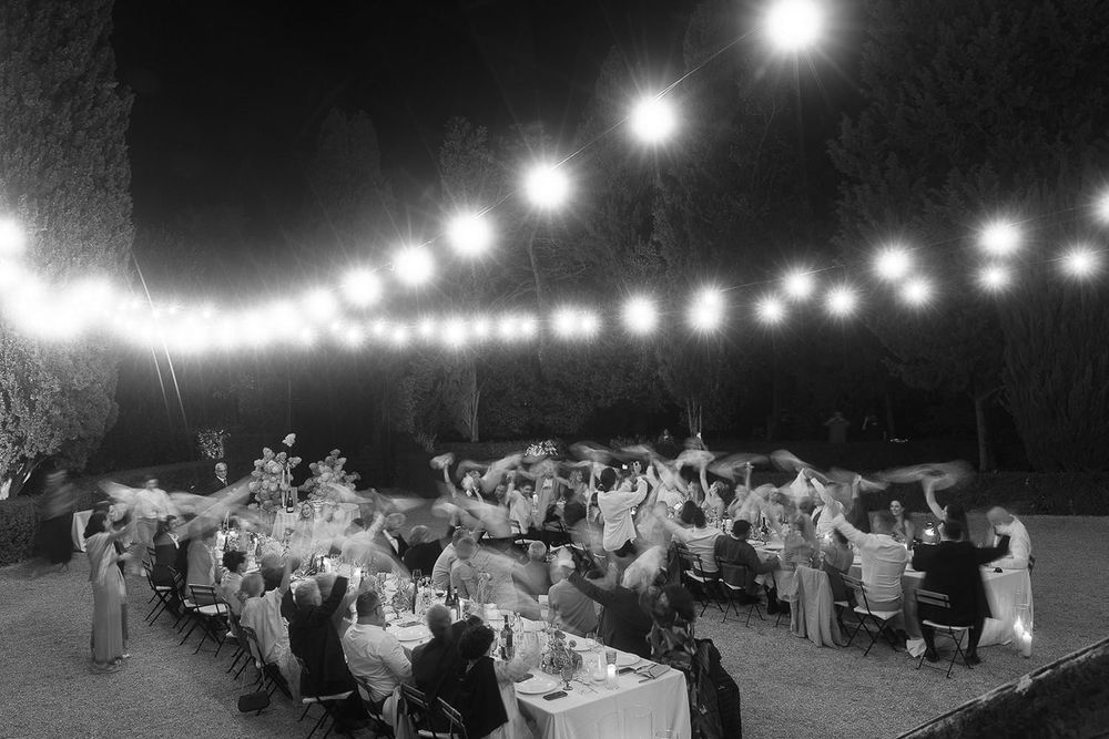 Black and white aerial view of outdoor wedding reception with string lights illuminating dining tables.