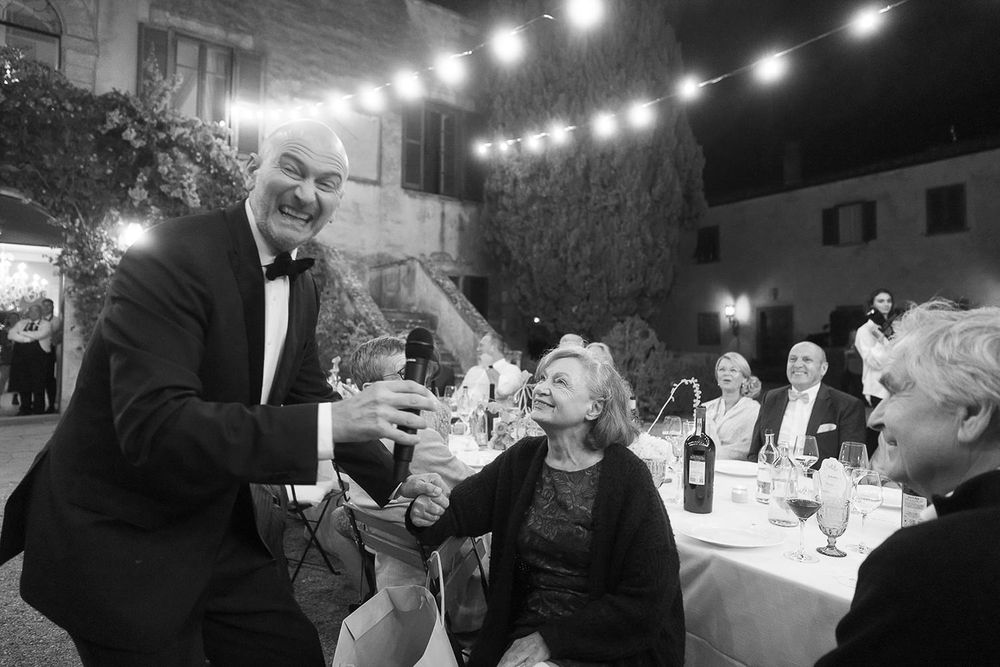 Guests enjoying drinks and laughter at an outdoor evening wedding reception under string lights.