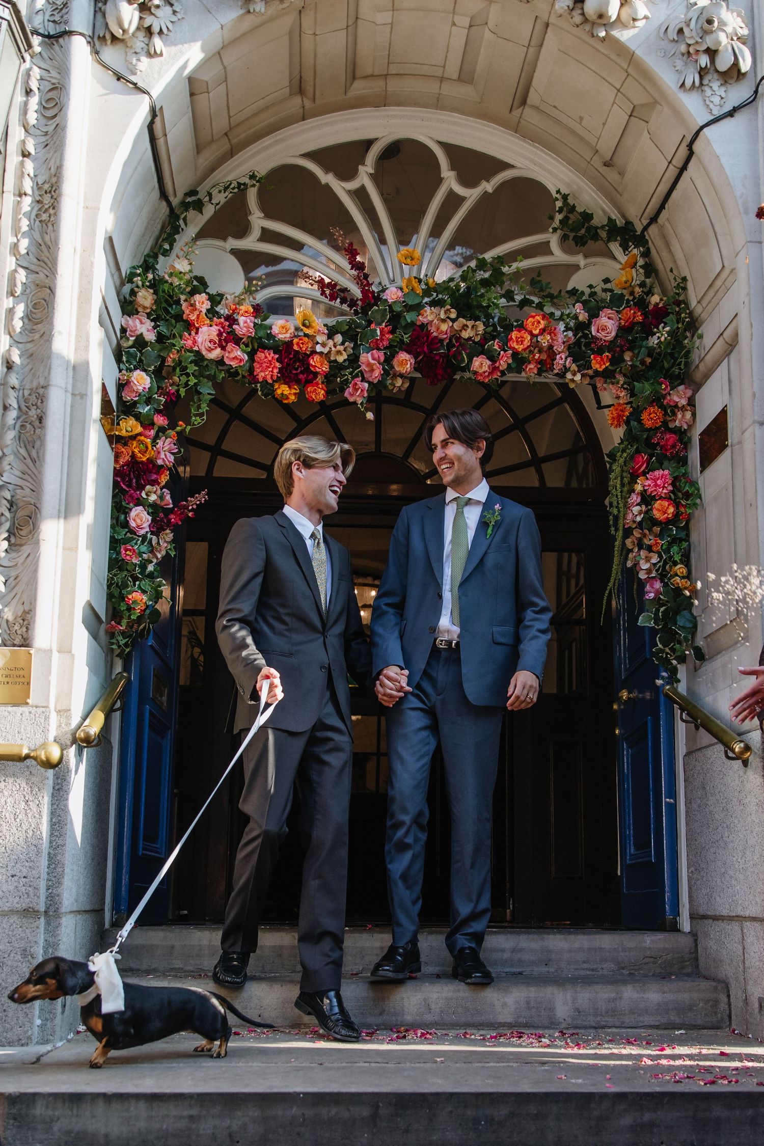 A couple stands under an ornate archway decorated with colorful flowers.