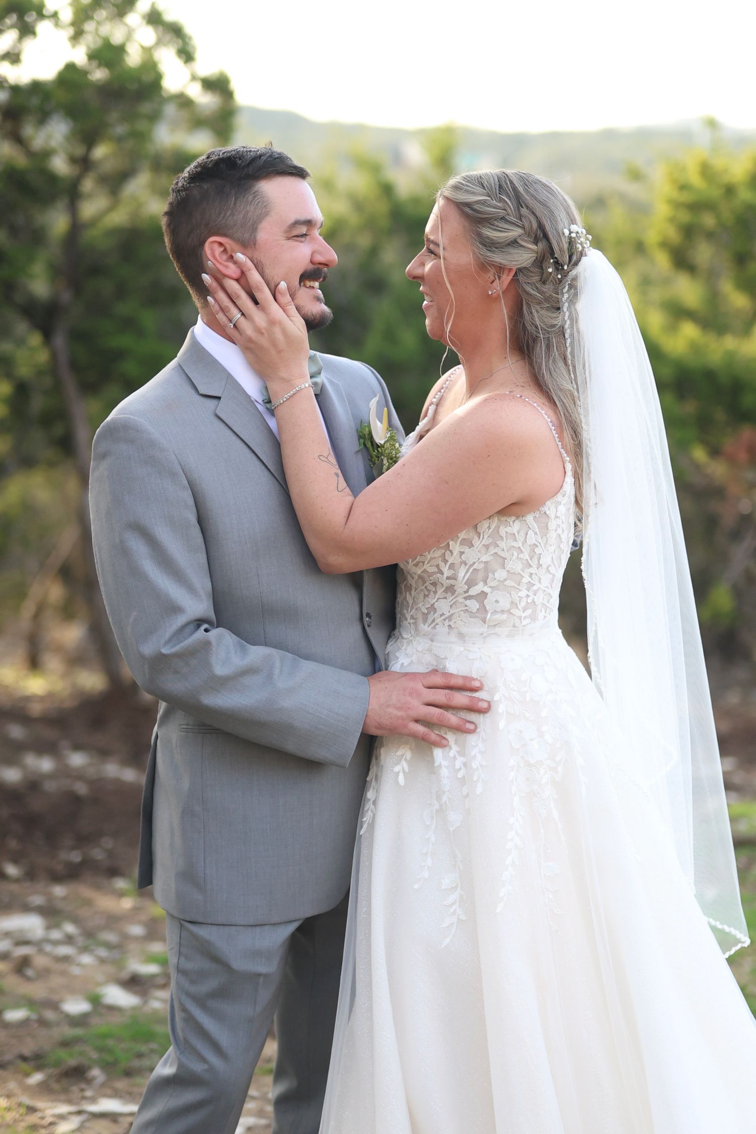 A joyful outdoor wedding moment shows a couple in gray suit and white dress sharing a tender moment at sunset.