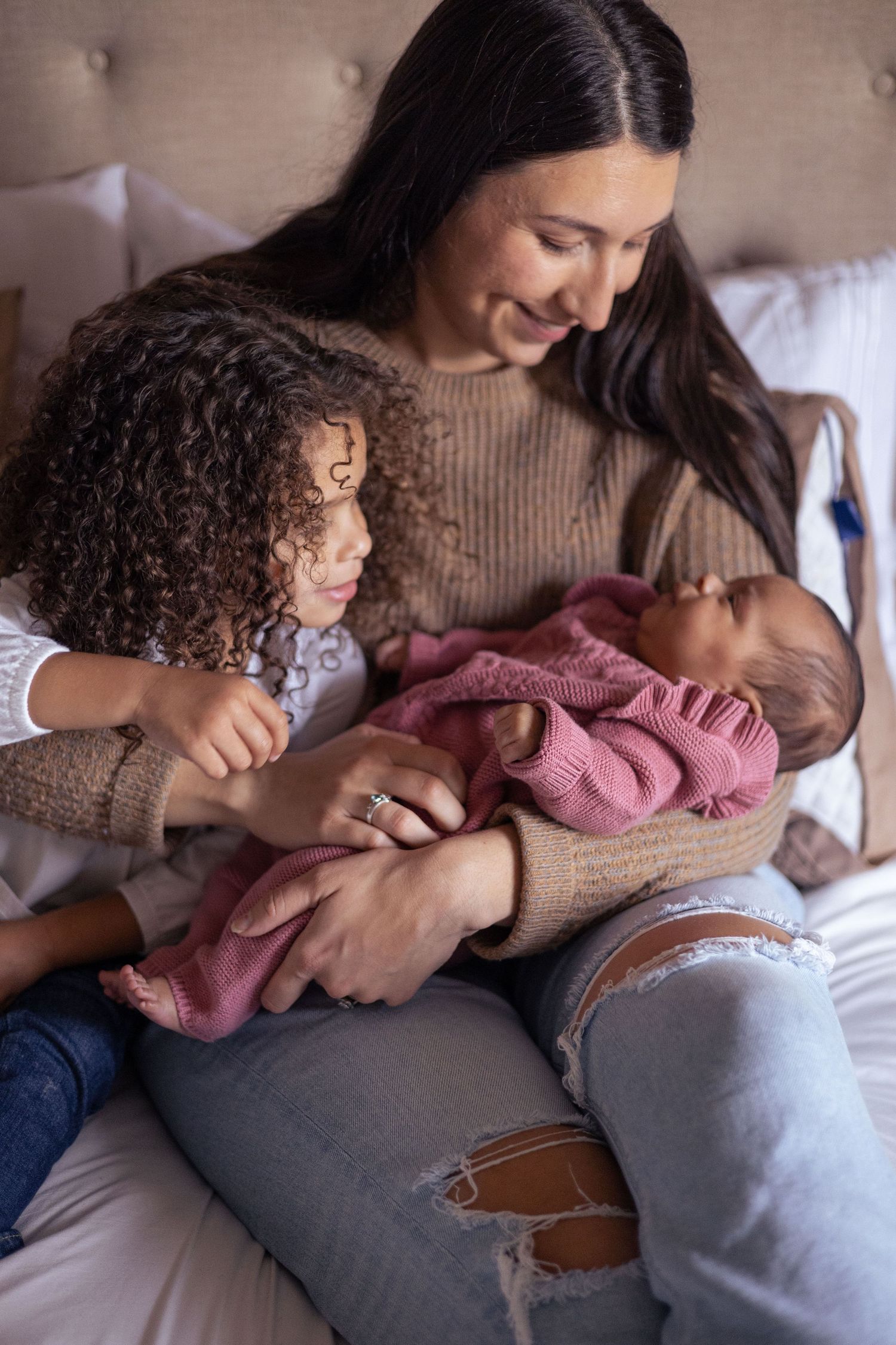 Mom and her toddler daughter look down at newborn baby.