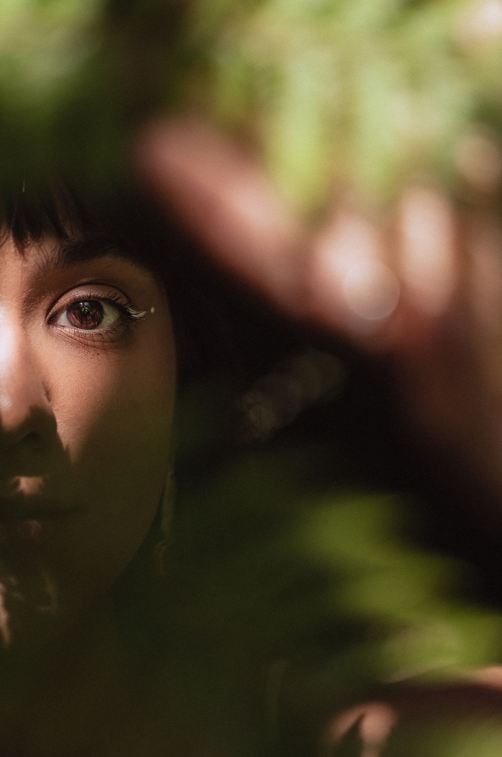 Close-up portrait through foliage showing half a face with dramatic shadows and natural lighting.