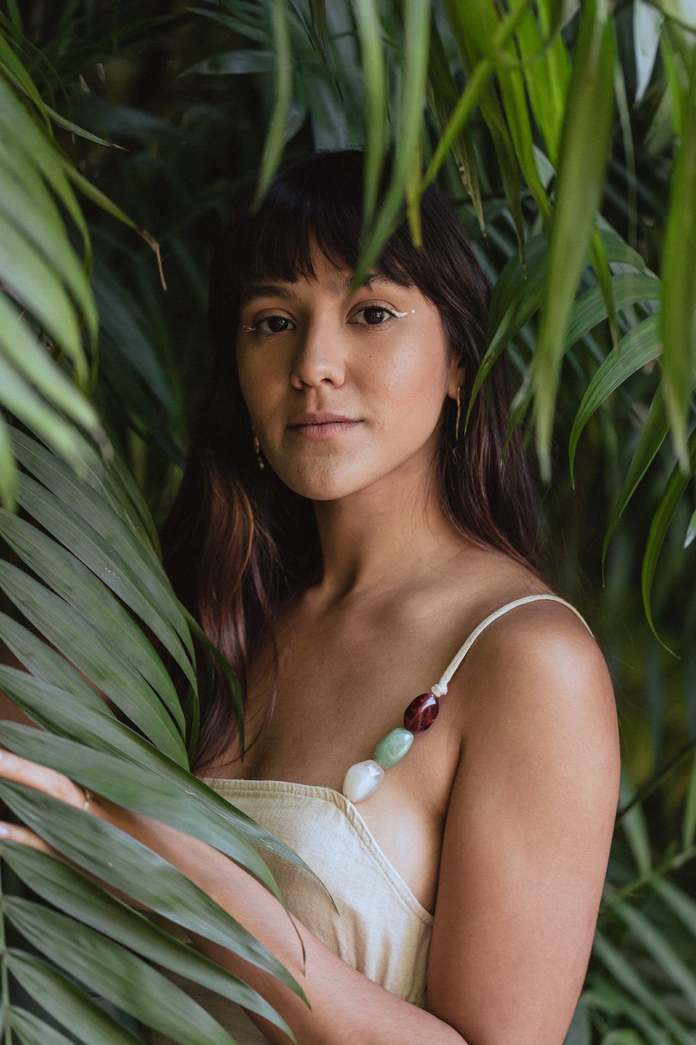 Portrait photograph with lush palm fronds framing a subject in a white top against a natural tropical background.